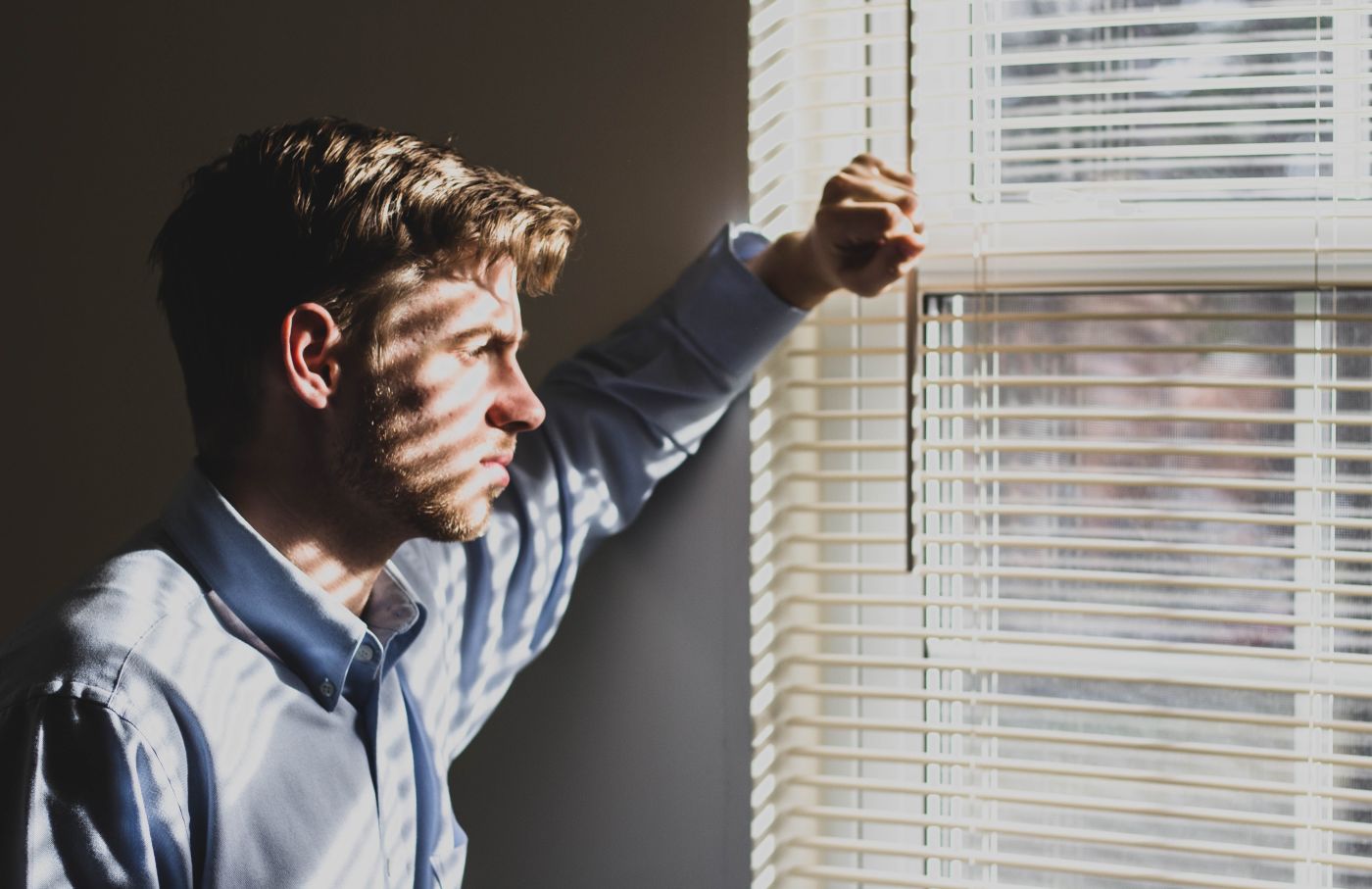 Man looking through blinds out a window